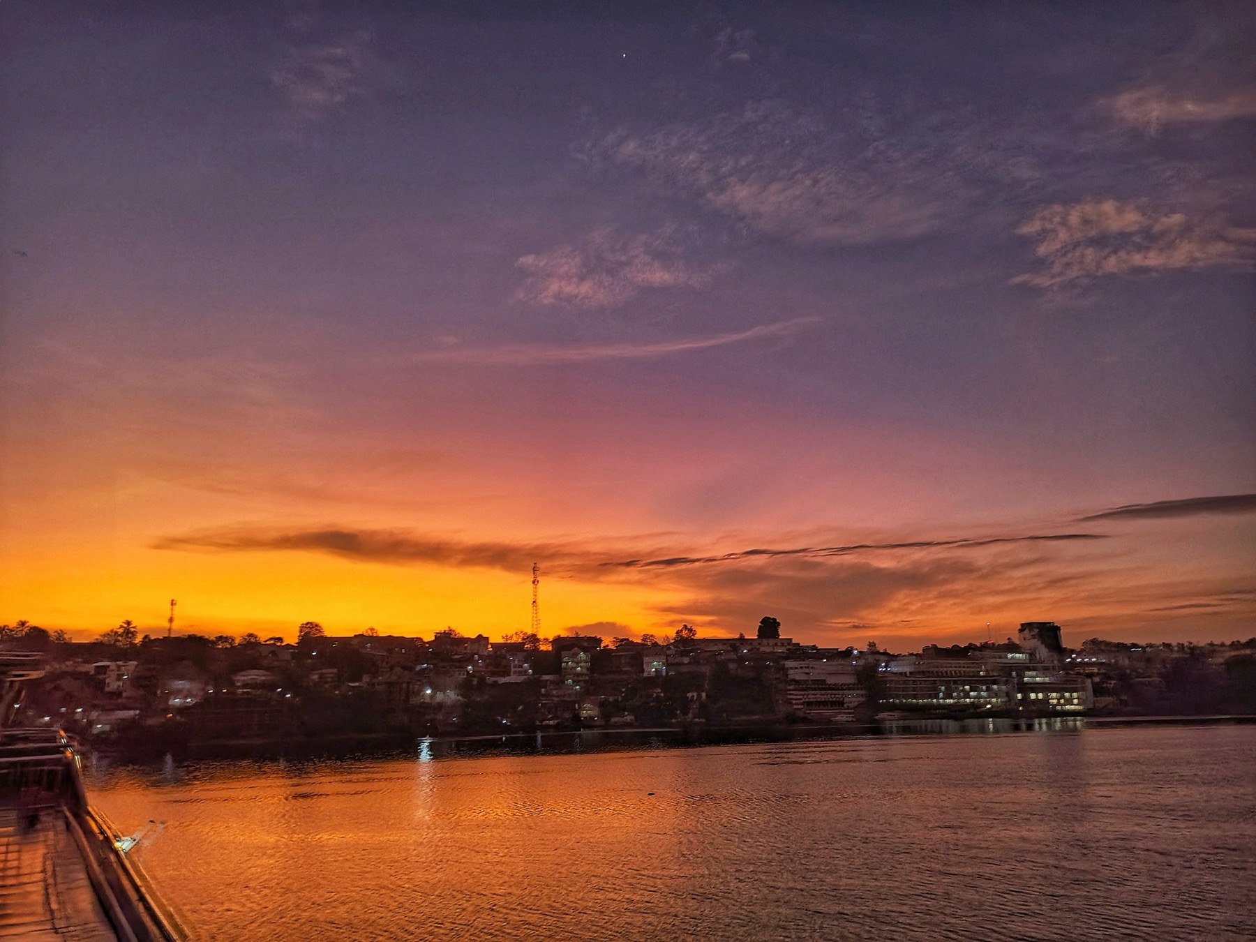 Bukavu's lakeside skyline in silhouette at dawn, with lit buildings and two tall masts, seen across Lake Kivu.